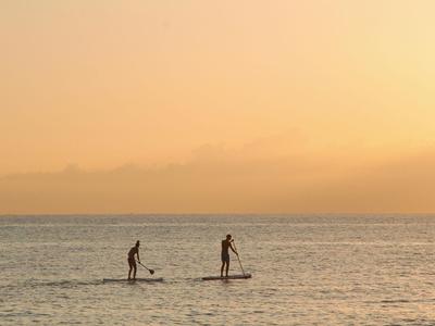 Due persone fanno paddleboarding sul mare al tramonto.