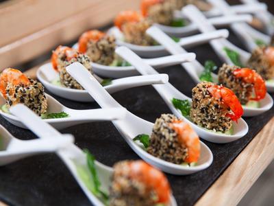 Vorspeisen mit Garnelen und Sesam auf weißen Löffeln, dekorativ auf schwarzer Platte arrangiert.