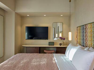 Gemütliches Hotelzimmer mit großem Bett, buntem Kopfteil und Flachbildfernseher an der Wand.