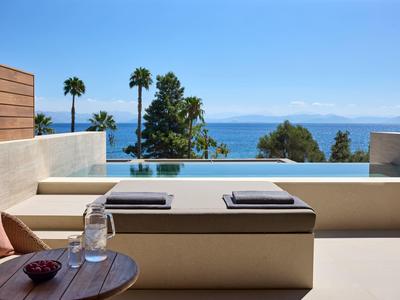 Moderner Hotelpool mit Meerblick, Liegen und einem kleinen Tisch mit Wasser und Schale.