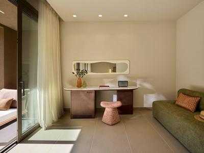 Moderner Hotelzimmer mit Schreibtisch, grüner Couch und direktem Zugang zu einer Terrasse.