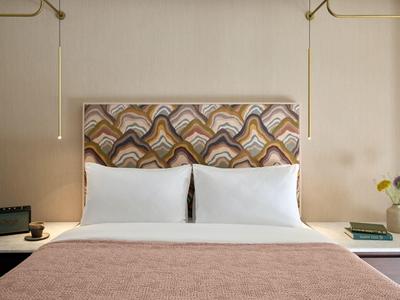 Modernes Hotelzimmer mit einem Doppelbett, gemustertem Kopfteil und seitlichen Nachttischen mit Lampen.