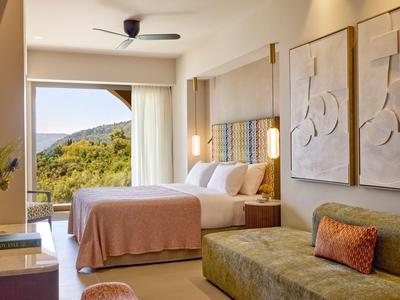 Helles Hotelzimmer mit Doppelbett, Sofa, Wandkunst und Blick auf grüne Hügel.