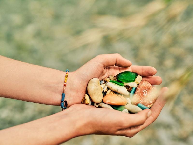 Zwei Hände halten bunte und natürliche Nüsse und Samen auf verschwommenem Hintergrund.