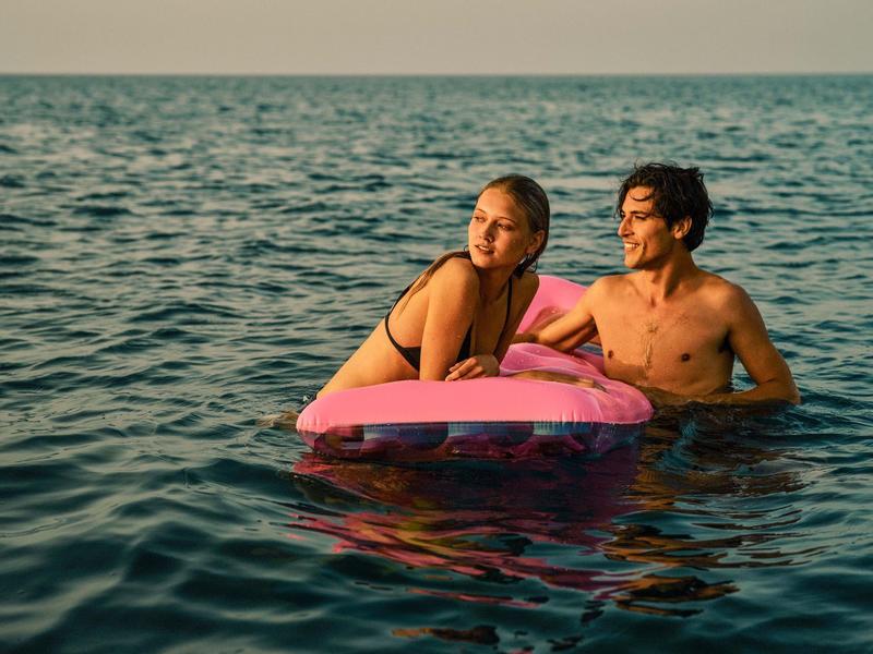 Zwei junge Leute im Wasser, die auf einem pinken Schwimmring entspannen, bei ruhiger See.