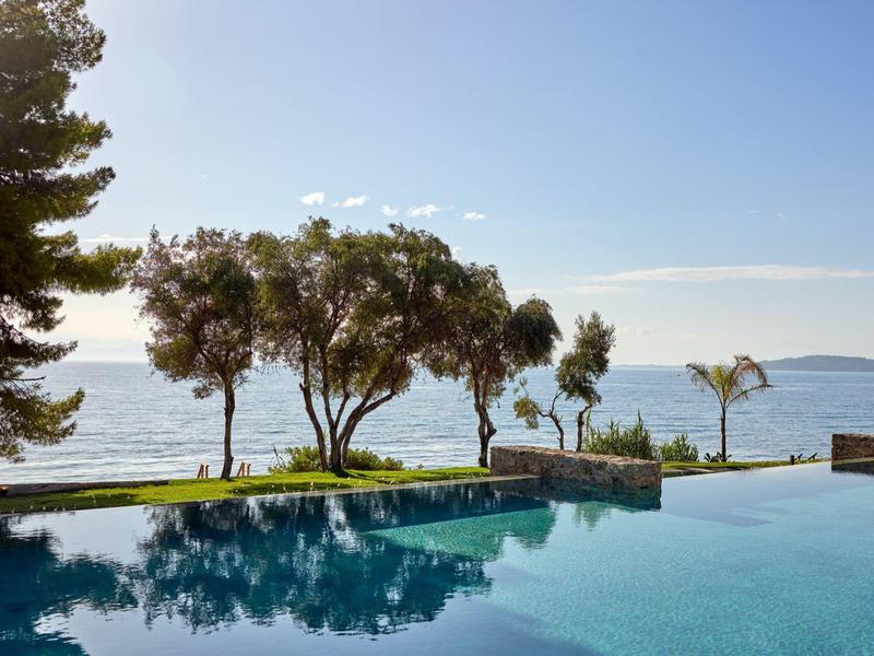 Infinity-Pool mit Blick auf ruhiges Meer und Bäume bei klarem Himmel.