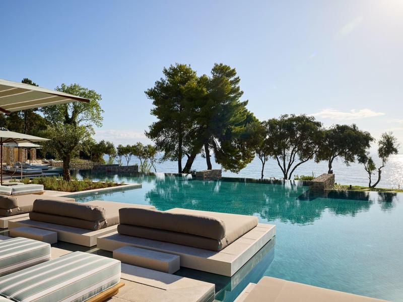 Luxuriöser Infinity-Pool mit Sonnenliegen und Meerblick bei klarem Himmel.