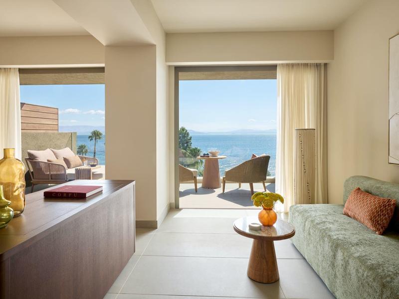 Helles Hotelzimmer mit Blick auf das Meer und einer Terrasse mit Sitzgelegenheiten.