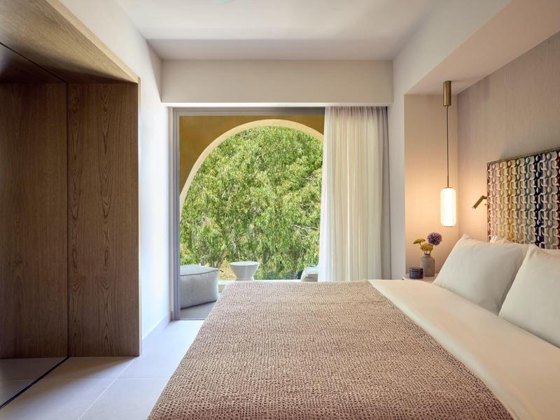 Modernes Hotelzimmer mit großem Bett, offenem Fenster und Blick ins Grüne.