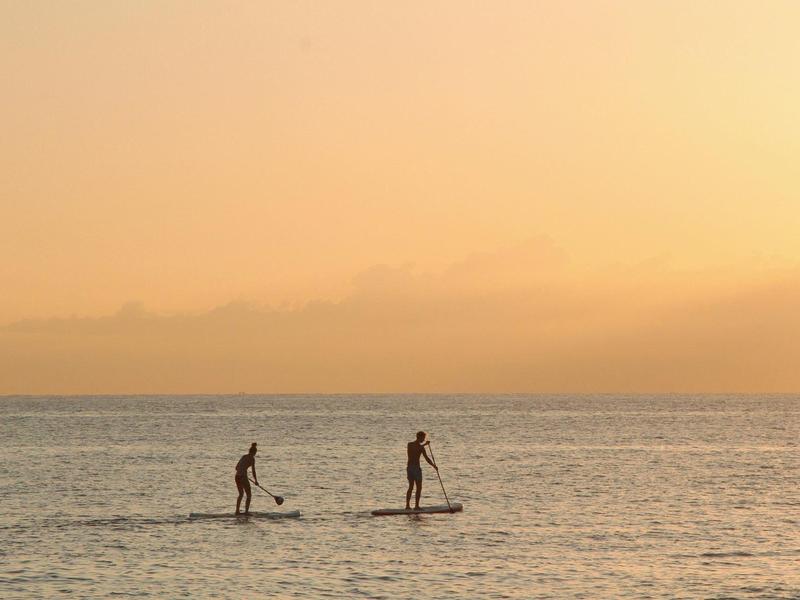 Zwei Menschen paddeln auf stehenden Boards im ruhigen Meer bei Sonnenuntergang.