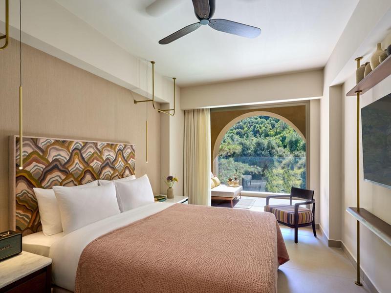 Helles Hotelzimmer mit großem Fenster, Doppelbett und Schreibtisch mit Blick auf die Natur.