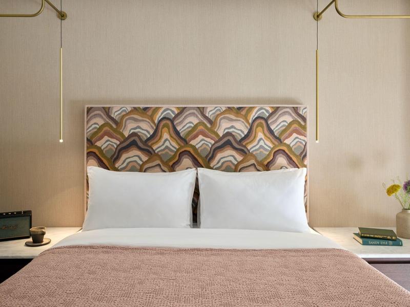 Modernes Hotelzimmer mit einem Doppelbett, gemustertem Kopfteil und seitlichen Nachttischen mit Lampen.