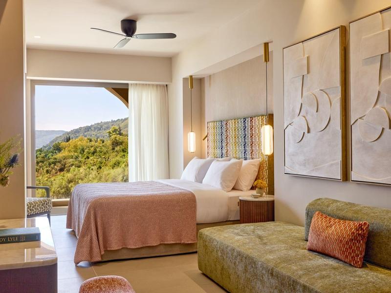 Helles Hotelzimmer mit Doppelbett, Sofa, Wandkunst und Blick auf grüne Hügel.