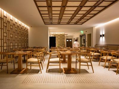 Moderner Gastraum mit Holztischen, Stühlen und warmen Lichtern in gedeckten Farben.