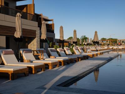 Reihe von Liegestühlen mit Sonnenschirmen neben einem Pool und Hotelgebäude bei klarem Himmel.