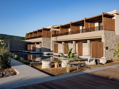 Modernes Hotelgebäude mit Holz- und Steinelementen, Terrasse und Pool unter klarem Himmel.