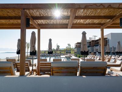 Sonnige Poolterrasse mit Liegestühlen und Sonnenschirmen an einem Hotel am Meer.