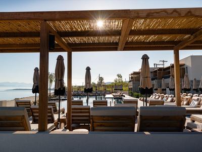 Outdoor-Poolbereich mit Liegestühlen, Sonnenschirmen und Blick auf das Wasser bei klarem Himmel.