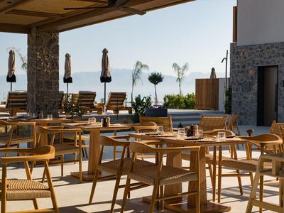 Leerer Außenbereich eines Restaurants mit Holzstühlen und Tischen, Sonnenschirmen und mediterranem Ambiente.