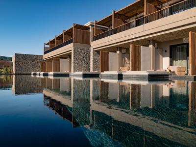 Modernes Hotel mit Überwasserbungalows und klar reflektierendem Pool bei blauem Himmel.
