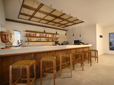 Moderner Barbereich mit Holztheke, Hockern und Regal mit diversen Flaschen an weißer Wand.