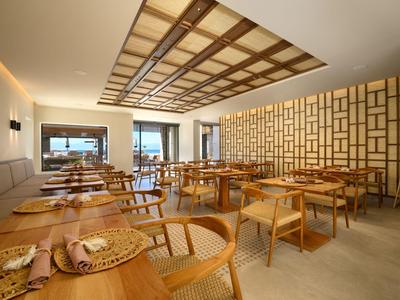 Modernes Restaurant mit Holztischen, Stühlen und dekorativem Wandmuster in hellem Raum.