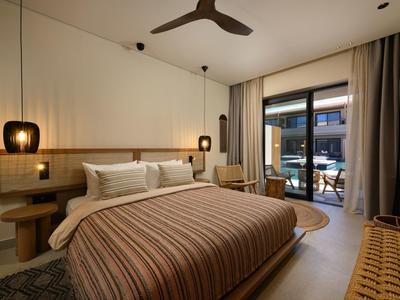 Modernes Schlafzimmer mit großem Bett, Holzdekor, zwei Hängeleuchten und Zugang zu Balkon mit Sitzbereich.