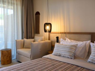 Gemütliches Hotelzimmer mit bequemen Sesseln, Bett mit gestreiften Kissen und sanfter Beleuchtung.