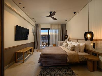 Modernes Schlafzimmer mit großem Bett, Fernseher, Deckenventilator und Balkon mit Meerblick.