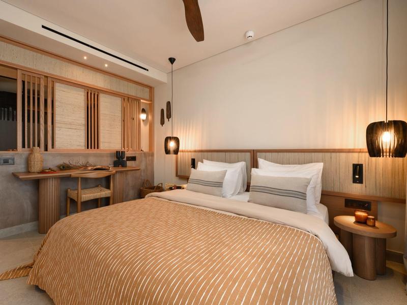 Modernes Schlafzimmer mit großem Bett, brauner Bettdecke, Holzmöbeln und warmem Licht.