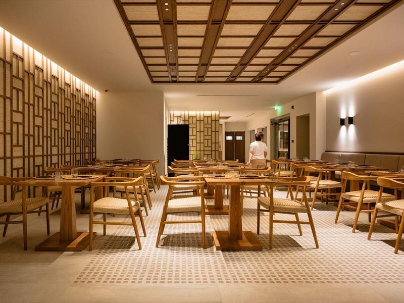 Moderner Gastraum mit Holztischen, Stühlen und warmen Lichtern in gedeckten Farben.