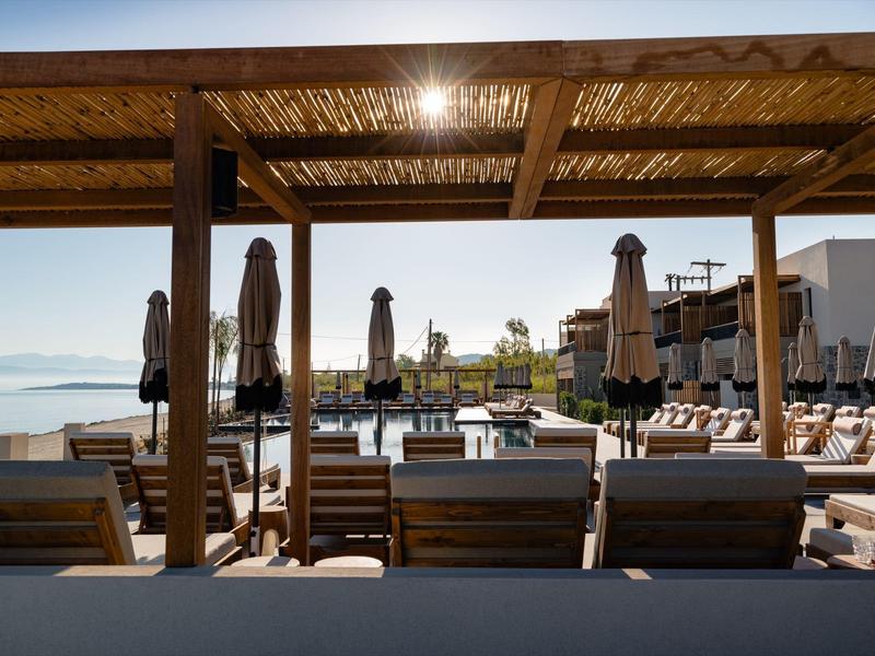 Outdoor-Poolbereich mit Liegestühlen, Sonnenschirmen und Blick auf das Wasser bei klarem Himmel.