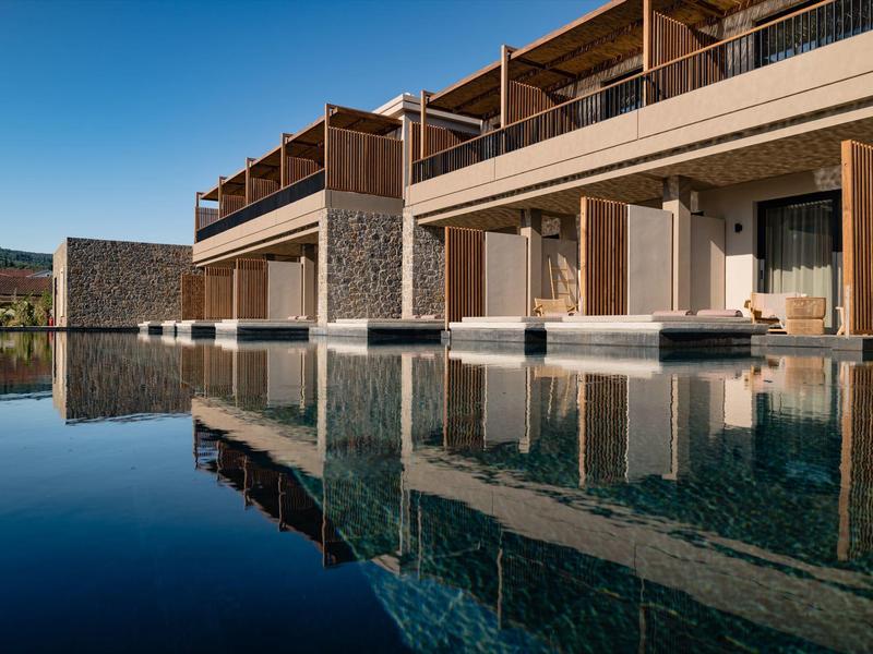 Modernes Gebäude mit Stein- und Holzelementen spiegelt sich klar im ruhigen Poolwasser.