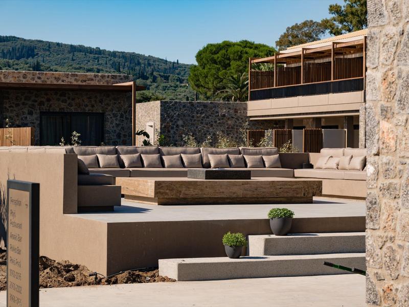 Moderner Außenbereich mit großen, grauen Sitzpolstern und niedrigen Grünpflanzen vor Gebäuden.