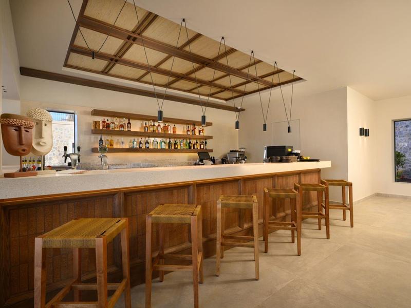 Moderner Barbereich mit Holztheke, Hockern und Regal mit diversen Flaschen an weißer Wand.