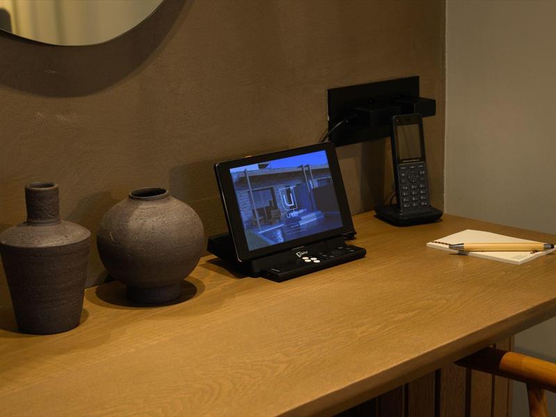 Holztisch mit zwei Keramikvasen, Tablet, Telefon und Stift auf hell beleuchtetem Hintergrund.