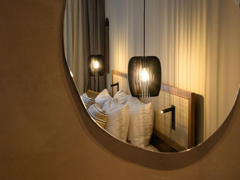 Spiegelbild eines gemütlichen Bettes mit weißen Kissen, Holzpaneel und warmem Licht der Lampe.