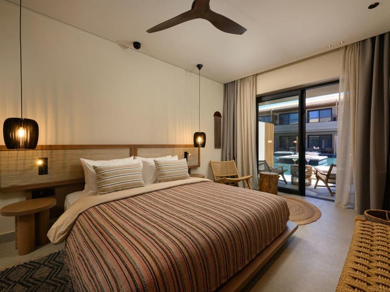 Modernes Schlafzimmer mit großem Bett, Holzdekor, zwei Hängeleuchten und Zugang zu Balkon mit Sitzbereich.