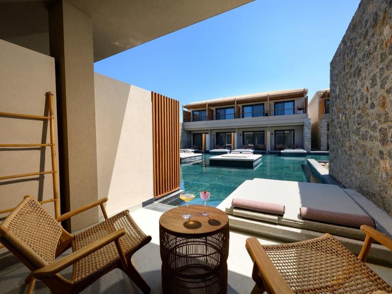 Innenhof mit Pool, moderner Lounge-Bereich mit Holzstühlen, Liegen und Steinmauer bei sonnigem Wetter.