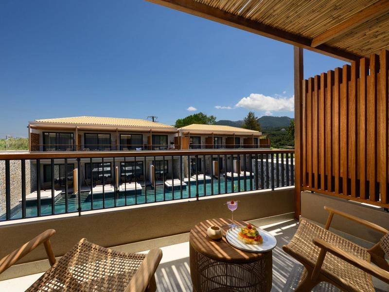 Balkon mit Korbsesseln und Tisch, Blick auf großzügigen Pool und moderne Gebäude.