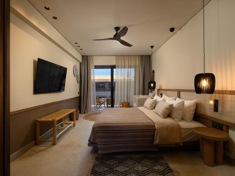 Modernes Schlafzimmer mit großem Bett, Fernseher, Deckenventilator und Balkon mit Meerblick.