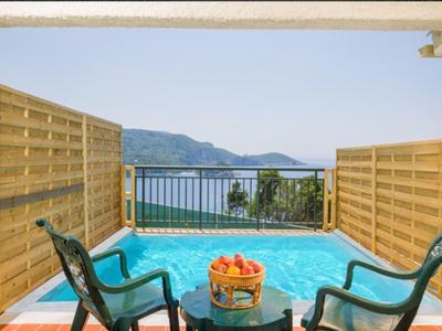 Een klein zwembad op een terras met uitzicht op zee, omgeven door houten schermen en twee stoelen.