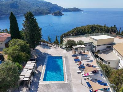 Blick auf einen Pool mit Sonnenschirmen und Liegestühlen, umgeben von Gebäuden und Meerblick.