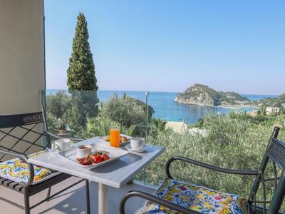 Balkon met twee stoelen, tafel met ontbijt, uitzicht op zee en eiland bij heldere lucht.