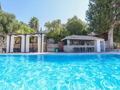 Grand piscine avec eau claire et bar de piscine dans un jardin vert et ensoleillé.