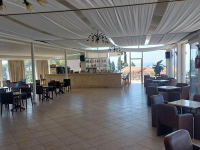 Grande salle à manger lumineuse avec de nombreuses tables et chaises, fenêtres panoramiques avec vue.