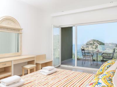 Chambre lumineuse avec lit double, bureau et balcon avec vue sur la mer.