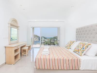 Lichte, moderne slaapkamer met groot bed, bureau en uitzicht op tuin en zwembad.