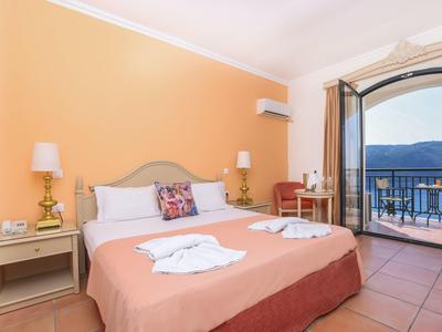 Lichte hotelkamer met tweepersoonsbed, tafel, stoel en balkon met uitzicht op de bergen.