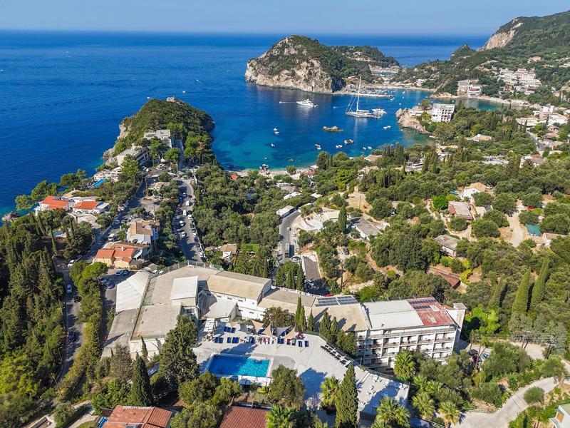 Luchtfoto van een kustplaats met hotels, groene vegetatie en blauwe zee op de achtergrond.